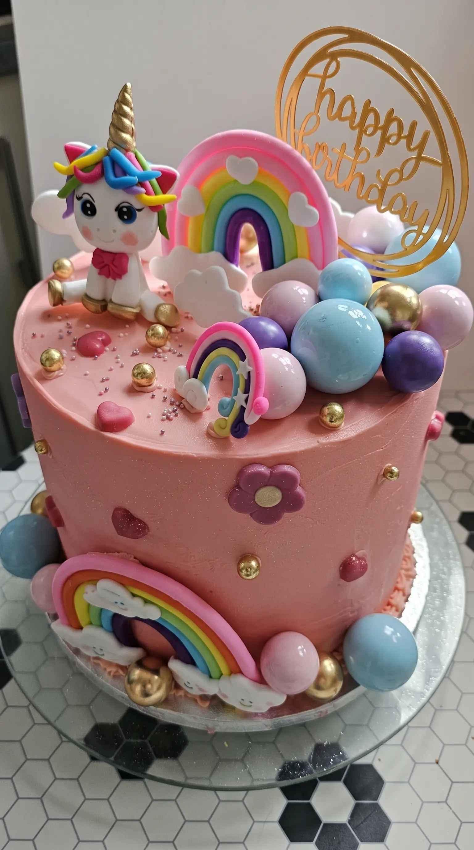 Pink children’s birthday cake decorated with a unicorn, rainbow details, pastel bubbles and gold accents